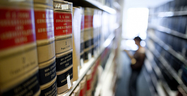 Library stacks with student reading in the background.
